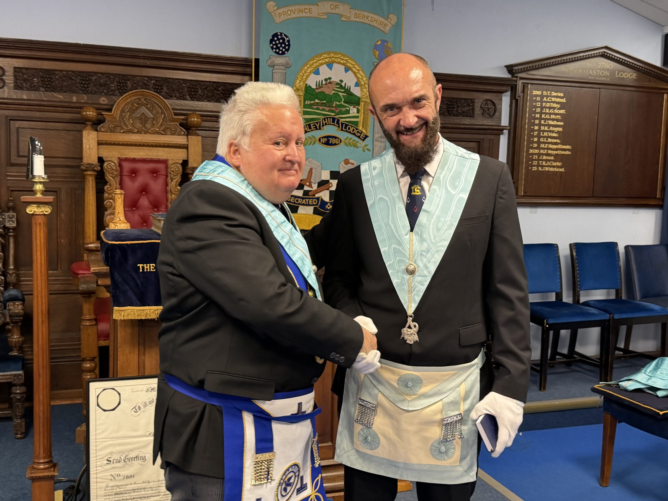 Two Brethren shaking hands in the lodge room, the Ashley Hill banner behind them